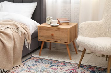 Yatağın yanında kahve, kitap ve çalar saat olan komodinin yanında.