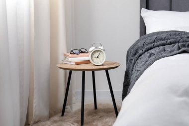 Yatağın yanında çalar saati, kitapları ve bardakları olan bir komodin.