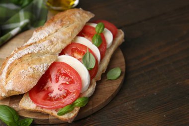 Mozarella peynirli, domatesli ve ahşap masadaki fesleğenli lezzetli sandviç, yakın plan. Metin için boşluk