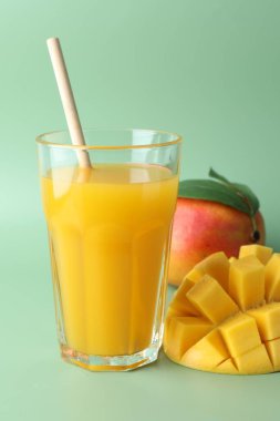 Bardakta lezzetli mango suyu ve yeşil arka planda taze meyve, yakın plan.