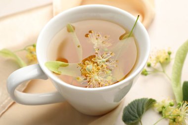 Fincanda taze ıhlamur çayı ve beyaz masada çiçekler, yakın plan.