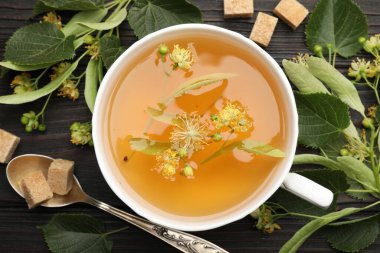 Taze ıhlamur çayı, şeker küpleri ve çiçekler koyu ahşap masada, düz uzanmış