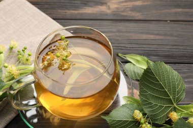 Fincanda taze ıhlamur çayı ve koyu ahşap masada çiçekler, yakın plan.