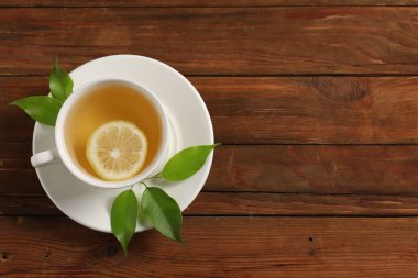 Lezzetli yeşil çay, fincanda limon ve ahşap masa yaprakları, üst manzara. Metin için boşluk
