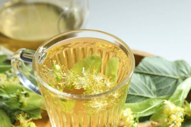 Fincanda lezzetli ıhlamur çayı, ışık masasında yapraklar ve çiçekler, yakın plan.