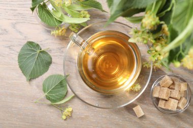 Fincanda nefis ıhlamur çayı, küp şekerler, yapraklar ve çiçekler ahşap masada, düz uzanmış