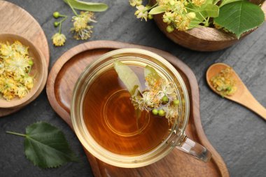 Lezzetli ıhlamur çayı fincanda, kaşıkta, yapraklarda ve çiçeklerde koyu dokulu masada, düz yerde.