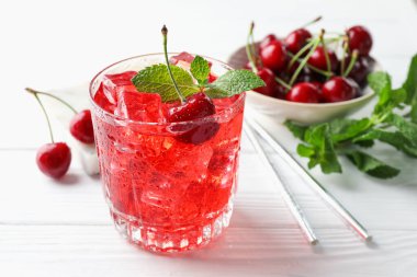 Buzlu vişneli gazoz, böğürtlen ve nane şekeri beyaz ahşap masada, yakın plan.