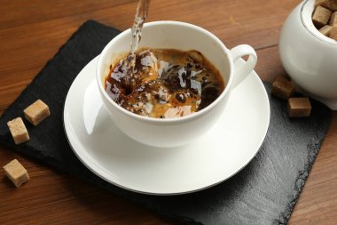 Bardağa sıcak su dökerek, hazır kahveyle ahşap masaya, yakın çekim.