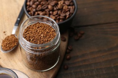 Cam kavanozda anında kahve ve ahşap masada fasulye, yakın plan. Metin için boşluk