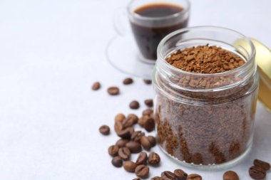 Cam kavanozdaki anlık kahve, fasulye ve sıcak içecek açık gri masada, yakın plan. Metin için boşluk