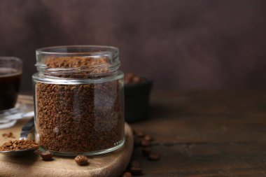 Cam kavanozda anında kahve ve ahşap masada fasulye, yakın plan. Metin için boşluk