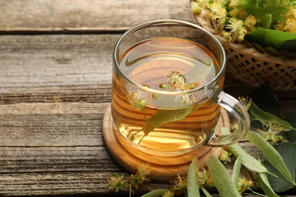 Fincanda lezzetli ıhlamur çayı, ahşap masada yapraklar ve çiçekler, yakın plan. Metin için boşluk