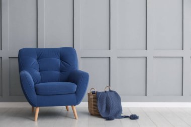 Rahat mavi koltuk ve sepet. Açık gri duvarın yanında kumaş var. Kapalı.