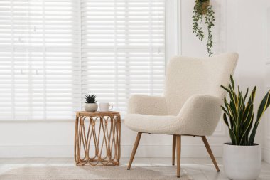 Rahat koltuk, yan masa ve beyaz duvarın yanındaki bitkiler.