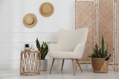 Rahat koltuk, yan masa ve beyaz duvarın yanındaki bitkiler.