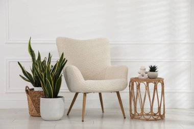 Rahat koltuk, yan masa ve beyaz duvarın yanındaki bitkiler.