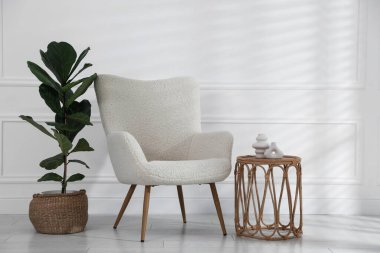 Rahat koltuk, yan masa ve beyaz duvarın yanındaki bitki örtüsü.