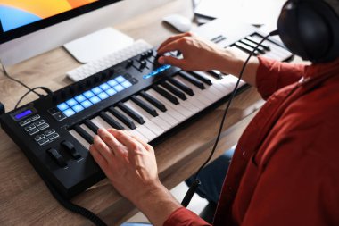 İçerideki ahşap masada MIDI klavyesiyle çalışan bir adam.