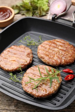 Ahşap masada lezzetli hamburger köfteleri ve baharatlar, yakın plan.