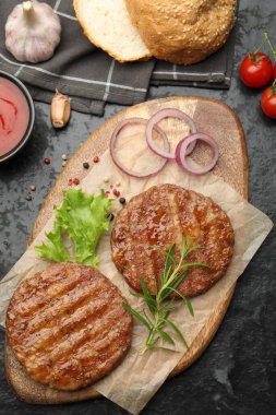 Lezzetli hamburger köfteleri, domatesler ve baharatlar siyah masada, düz yerde