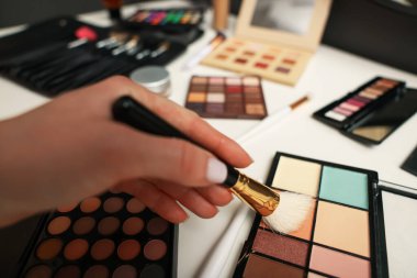 Makyaj masasında fırça ve kapatıcı paleti olan kadın, yakın plan.