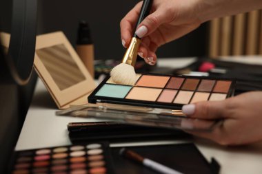 Makyaj masasında fırça ve kapatıcı paleti olan kadın, yakın plan.