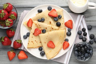 Böğürtlenli ve kremalı leziz krepler gri ahşap masada, düz yerde