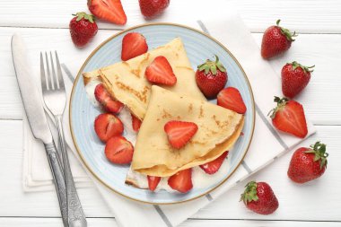 Beyaz ahşap masada çilekli ve kremalı leziz krepler.