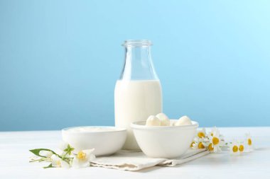 Taze süt ürünleri ve çiçekler beyaz ahşap masada açık mavi arka planda