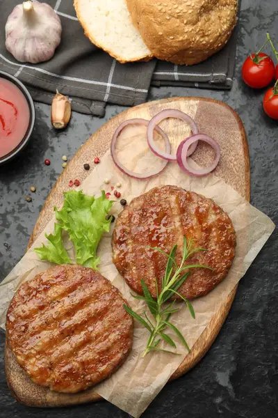 Lezzetli hamburger köfteleri, domatesler ve baharatlar siyah masada, düz yerde