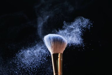 Siyah arkaplanda kozmetik ürünle makyaj fırçası, yakın plan