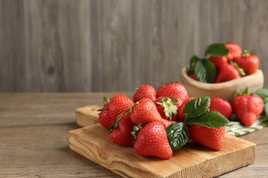 Ahşap masada lezzetli olgun çilekler ve yeşil yapraklar, yakın plan. Metin için boşluk