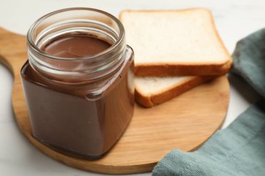 Cam kavanozda çikolatalı tereyağı ve beyaz masada dilimler, yakın plan.