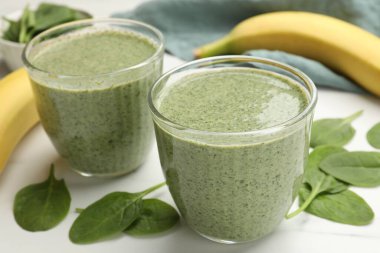 Lezzetli ıspanaklı smoothie ve malzemeler beyaz masada, yakın plan.