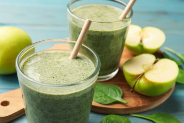 Lezzetli ıspanaklı smoothie ve açık mavi ahşap masa üzerindeki malzemeler, yakın plan.