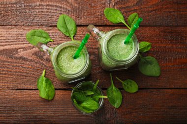 Duvarcı kavanozunda nefis bir smoothie ve ahşap masada ıspanak yaprakları.
