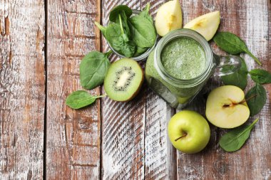 Mason kavanozunda leziz bir smoothie, ıspanak yaprakları, elma ve kivi renkli ahşap masa, düz yatak