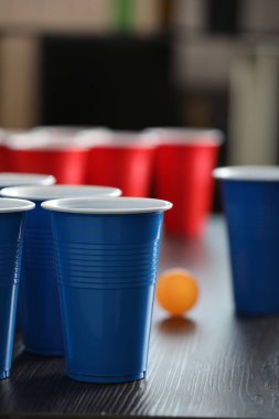 Bira pong oyunu. İçkili plastik bardaklar ve tahta masada top, yakın plan.