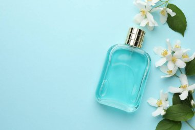 Bir şişe parfüm, güzel yasemin çiçekleri ve açık mavi arka planda yeşil yapraklar. Metin için boşluk
