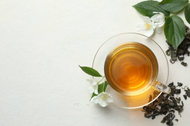 Cam bardakta Aromatik yasemin çayı, beyaz masada çiçekler ve yapraklar, düz uzanmış. Metin için boşluk