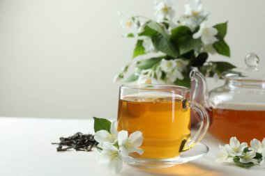 Cam bardakta yasemin çayı, çaydanlık, çiçekler ve kuru yapraklar beyaz masada, yakın plan. Metin için boşluk