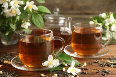 Cam fincanlarda yasemin çayı, çaydanlık, bira ve çiçekler ahşap masada, yakın plan.