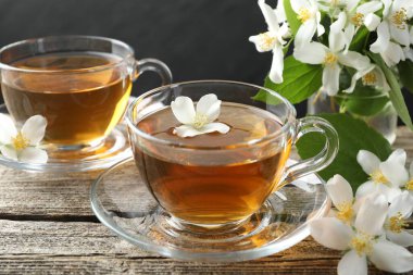 Cam fincanlarda yasemin çayı, tahta masada çiçekler ve yeşil yapraklar, yakın plan.