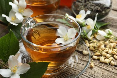 Cam bardaklarda yasemin çayı, ahşap masada bira ve çiçekler, yakın plan.