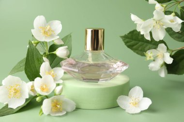 Yeşil arka planda bir şişe parfüm ve yasemin çiçeği, yakın plan.