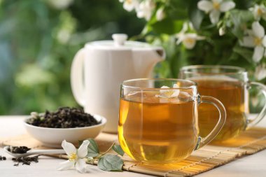 Lezzetli yasemin çayı fincanlar, çaydanlık, kuru yapraklar ve çiçekler beyaz ahşap masada, yakın plan.