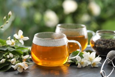 Bardakta lezzetli yasemin çayı, siyah masada kuru yapraklar ve çiçekler, yakın plan.