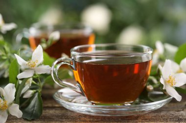 Lezzetli yasemin çayı fincanda ve çiçekler ahşap masada, yakın plan.