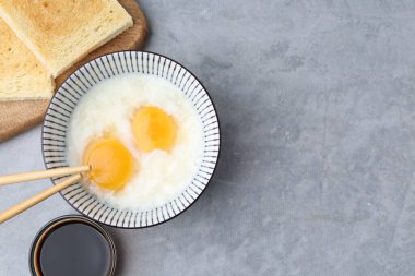 Geleneksel Asya kahvaltısı, yarı haşlanmış yumurta, soya sosu, ekmek ve çubuklar gri masada, düz yayla. Metin için boşluk